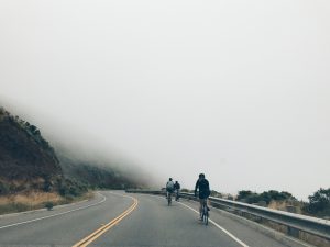 Three bikers on a foggy road near a cliff