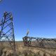 Crews working on a Natina-treated lattice tower with a crane lifting a steel section into place in mountainous terrain.