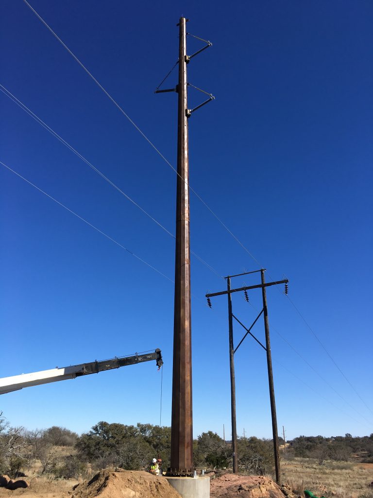 Natina-treated steel Natina-treated utility pole being installed for grid hardening with older wood structure in the background.
