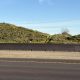 Desert hillside with wildlife crossing fencing and Natina-treated natural-looking roadside Zoneguard barrier along a highway corridor.